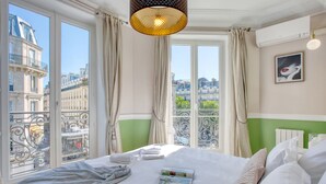 A hotel room with a large bed, a view of Paris buildings, and a balcony with wrought iron railings. - Charming 100m² with 3BR - Romantic City Center (Paris)
