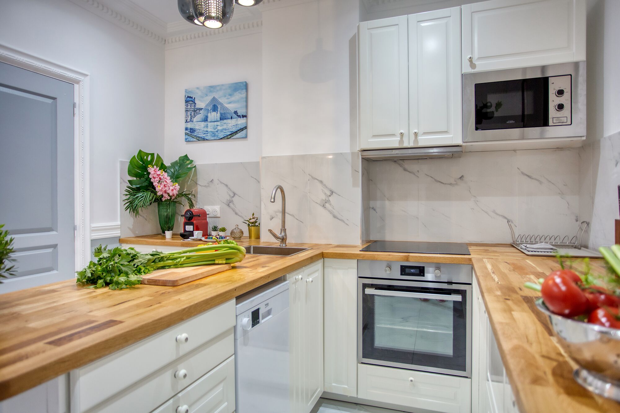 Une cuisine moderne avec des meubles blancs, un four encastré, un four à micro-ondes et un plan de travail en bois.