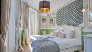 A bedroom with a bed, a bedside table, a lamp, and a window with curtains. - Charming 100m² with 3BR - Romantic City Center (Paris)