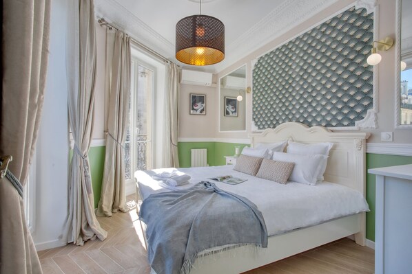 A bedroom with a bed, a bedside table, a lamp, and a window with curtains. - Charming 100m² with 3BR - Romantic City Center (Paris)