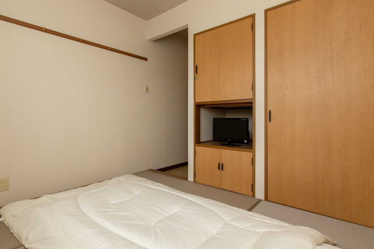 A bedroom with a bed, a television on a shelf, and wooden wardrobes.