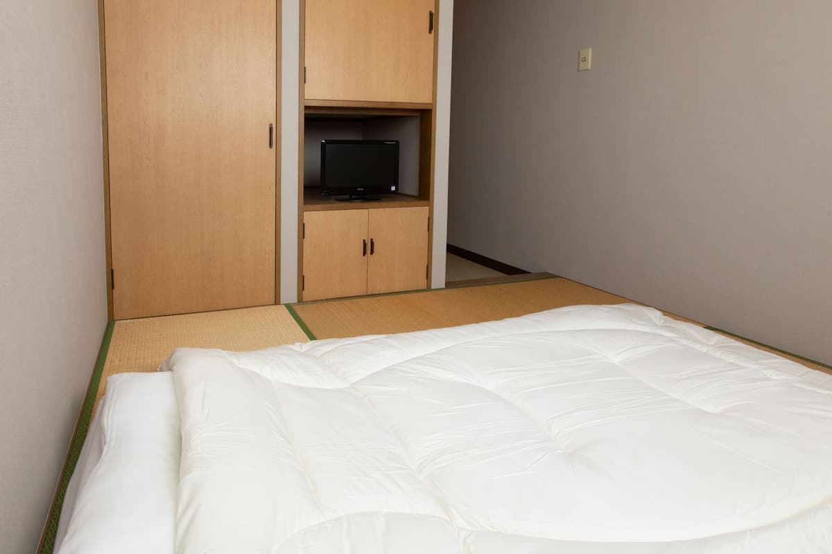 A room with a bed, a television on a shelf, and a wardrobe.