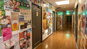 A hallway with wooden flooring, a door labeled '29', and walls covered with various posters and advertisements. - Tabist Business Ryokan Duck Ishinomaki Hebita (Isinomaki)