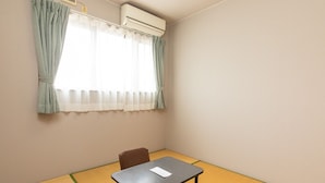 Een kleine kamer met een tatami vloer, een tafel, een stoel en een raam met gordijnen.
