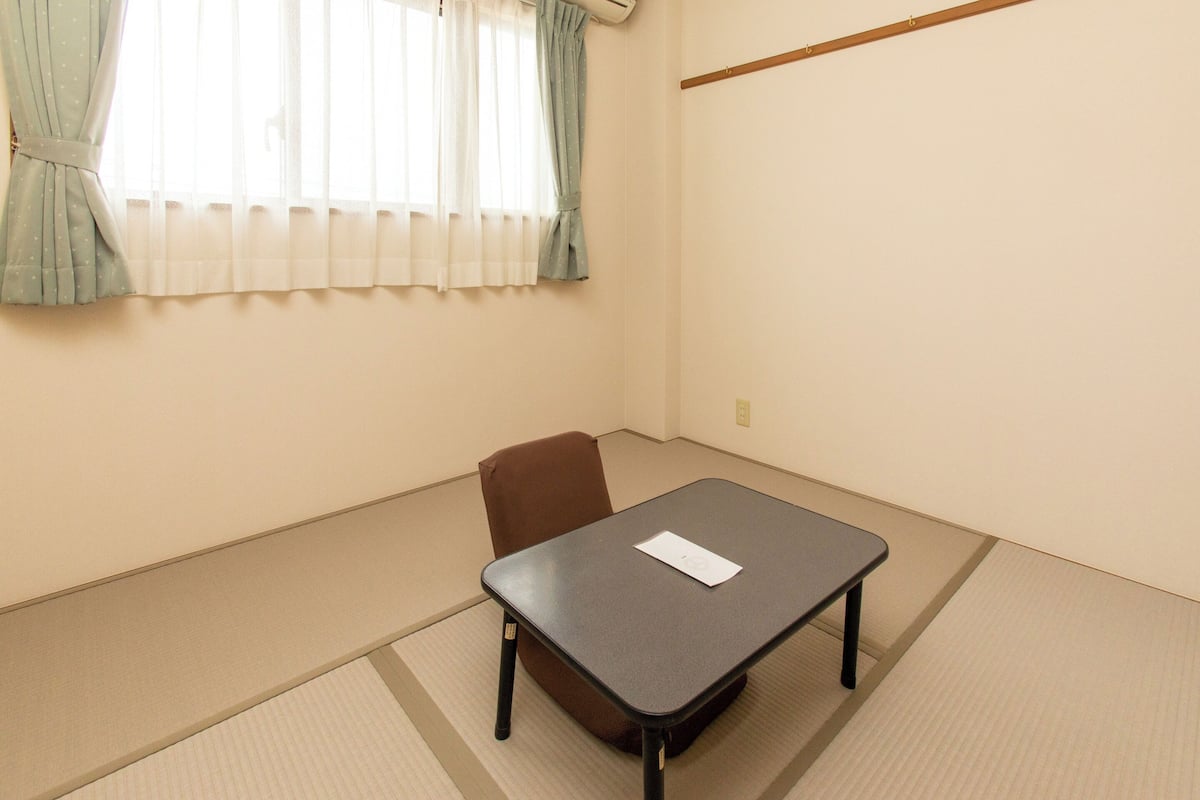 A room with tatami flooring, a table, a chair, and a window with curtains.