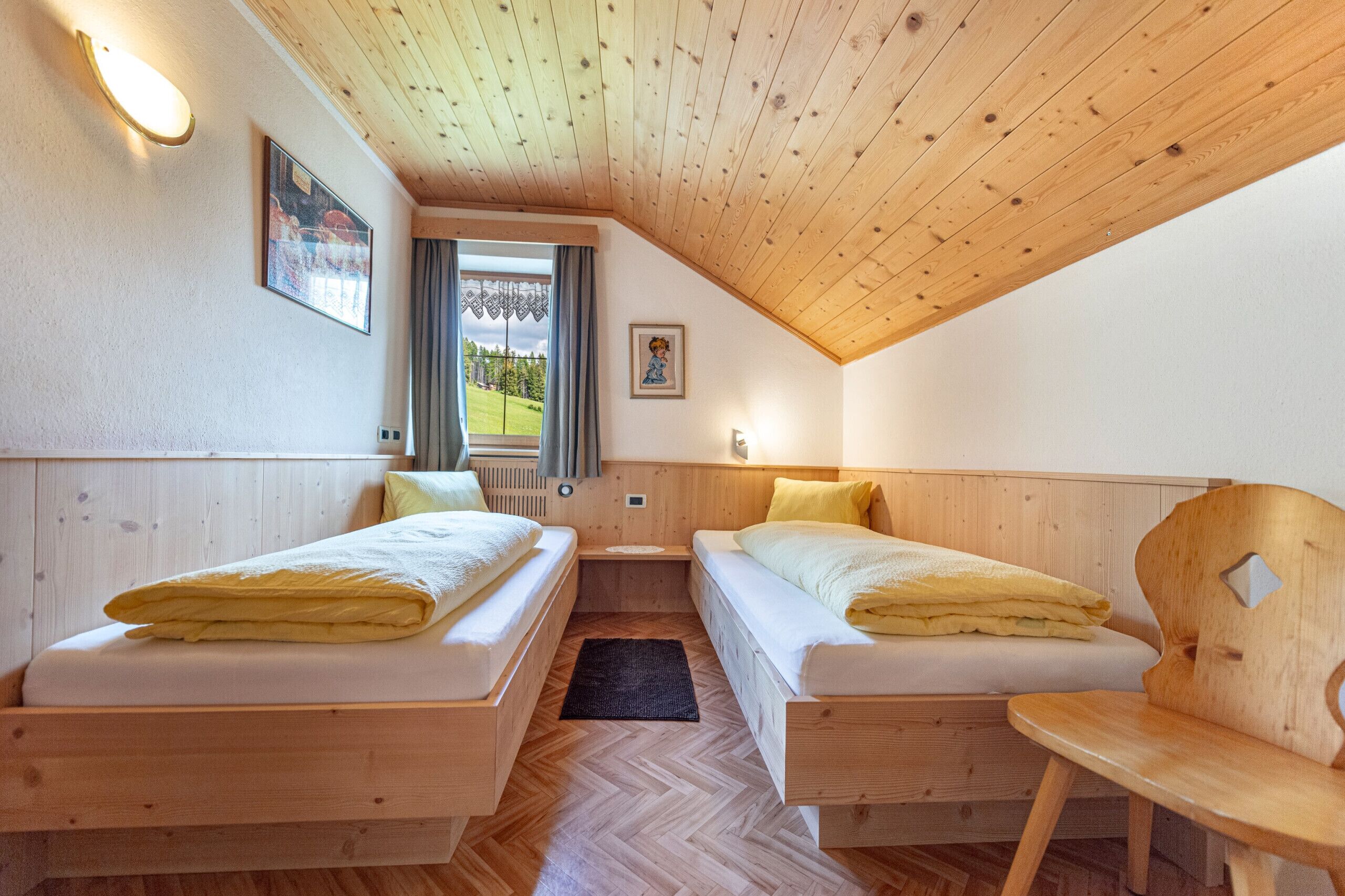 Une petite pièce chaleureuse, avec deux lits en bois, un plafond en bois et une fenêtre donnant sur un paysage verdoyant.