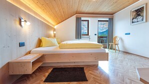 Quarto moderno com teto de madeira, cama com roupa de cama amarela, mesa de cabeceira pequena e vista para o exterior pela janela.