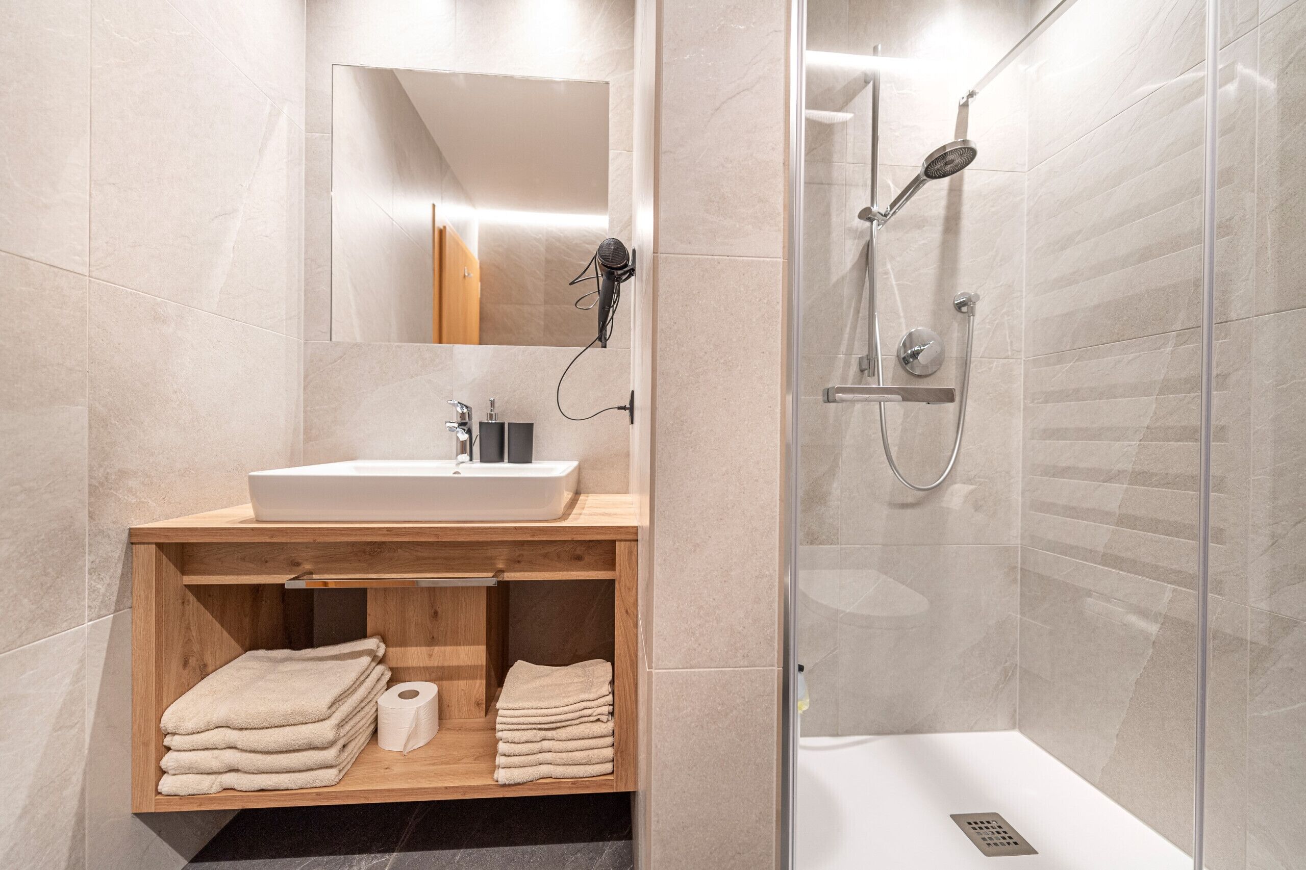 A modern bathroom with a wooden vanity, a sink, and a glass-enclosed shower.