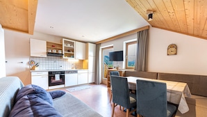 A modern kitchen with white cabinets, a dining area with a table and chairs, and a cozy seating area with a sofa and a bench. - Holiday Farm Al Cir 400B (San Martino in Badia)