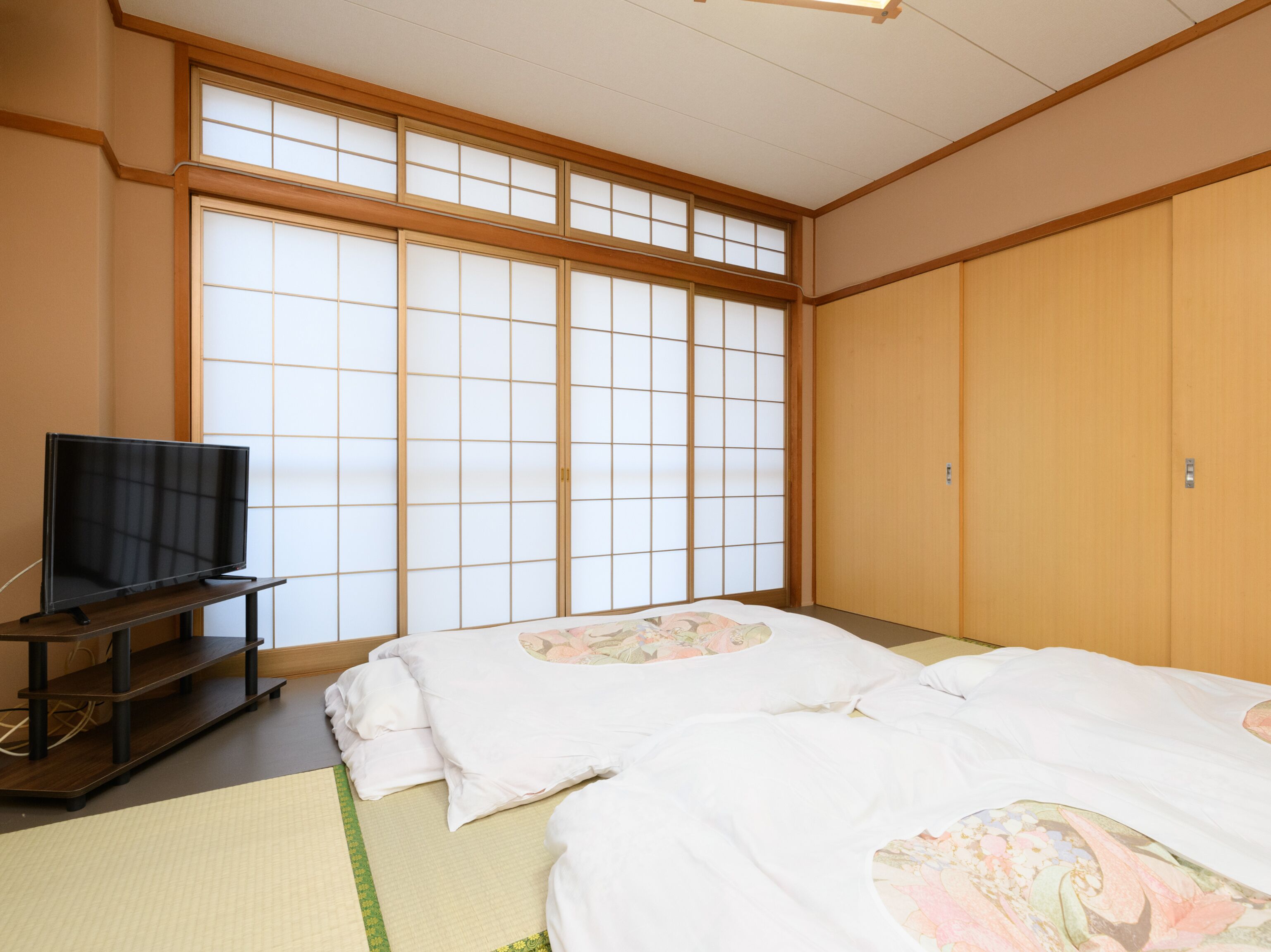 Een traditionele Japanse kamer met tatami vloerbedekking, een futon bed, een televisie op een lage standaard en schuifdeuren van shoji papier.