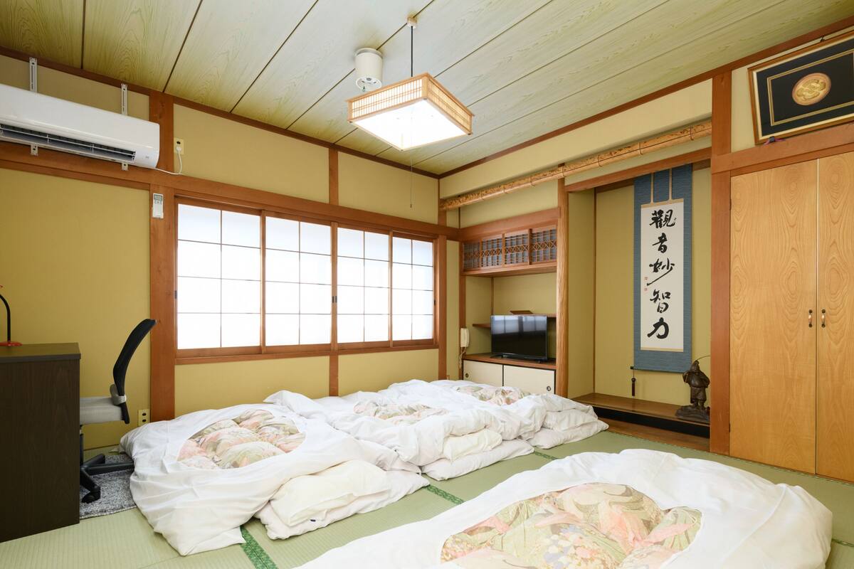 Une pièce de style japonais traditionnel, avec des tatamis au sol, un futon servant de lit, une télévision et un paravent en papier de riz (shoji).