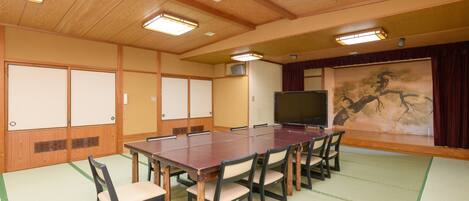 Un salón de conferencias con una larga mesa, sillas, un proyector y una pintura tradicional japonesa.