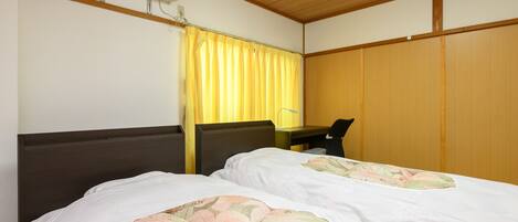 A hotel room with two beds, a desk, a chair, an air conditioning unit, and a curtain.