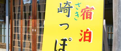 A yellow sign with Japanese characters, mounted on a metal frame, in front of a building with wooden doors and windows.