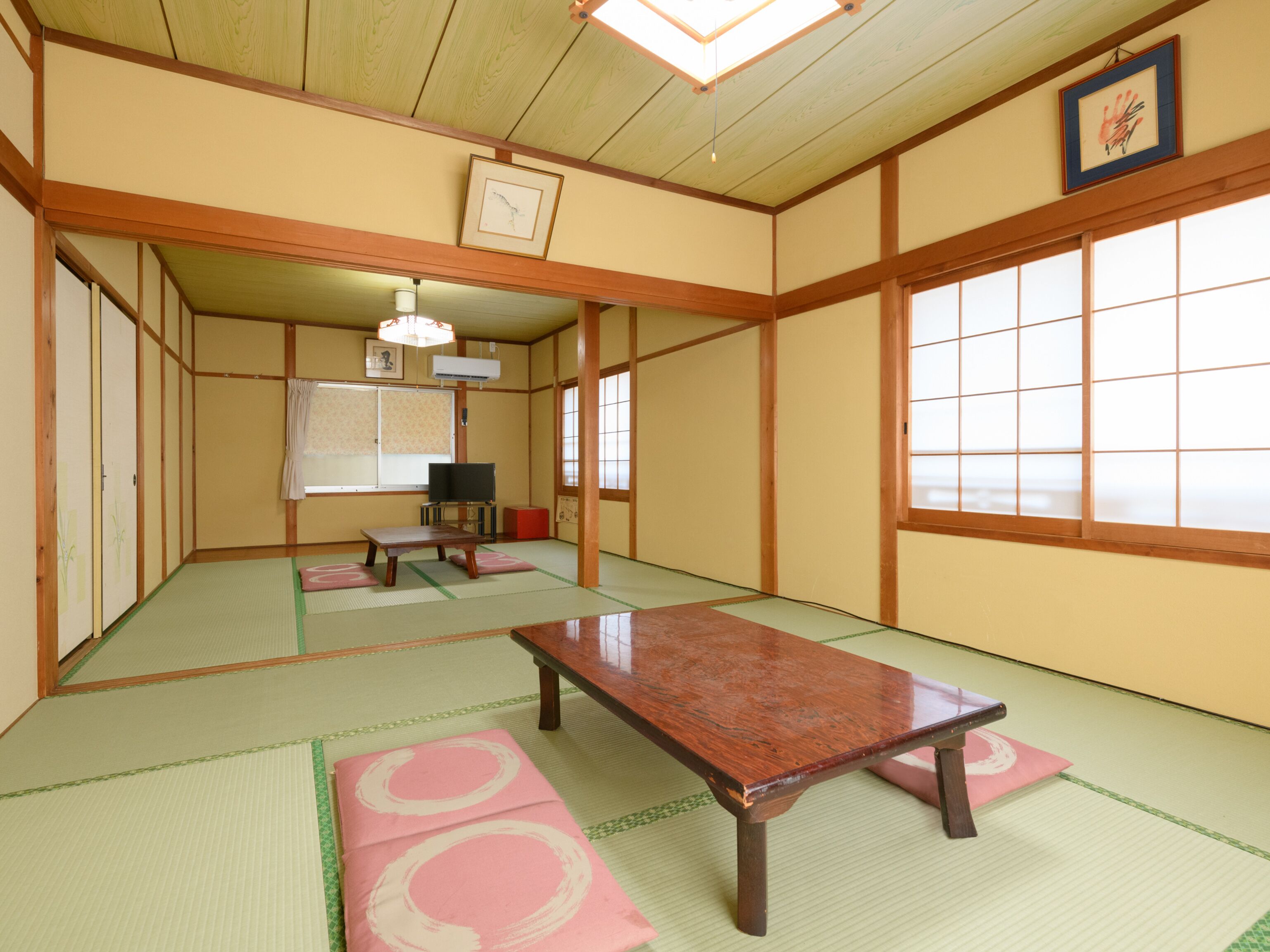 A traditional Japanese room with tatami flooring, a low wooden table, a TV, and sliding doors.