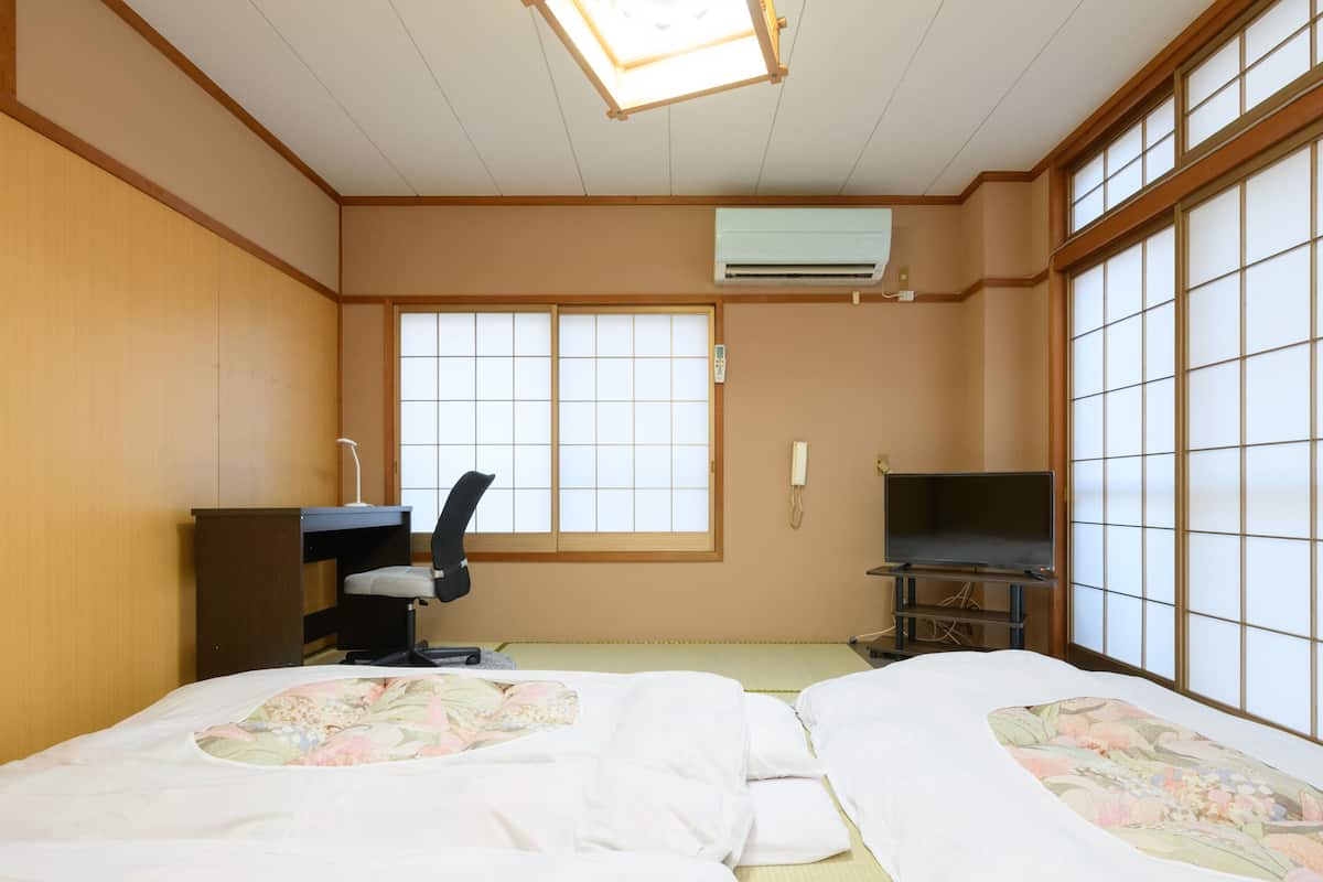 Une chambre d’hôtel avec deux lits, un bureau, une chaise, une télévision et une grande fenêtre.