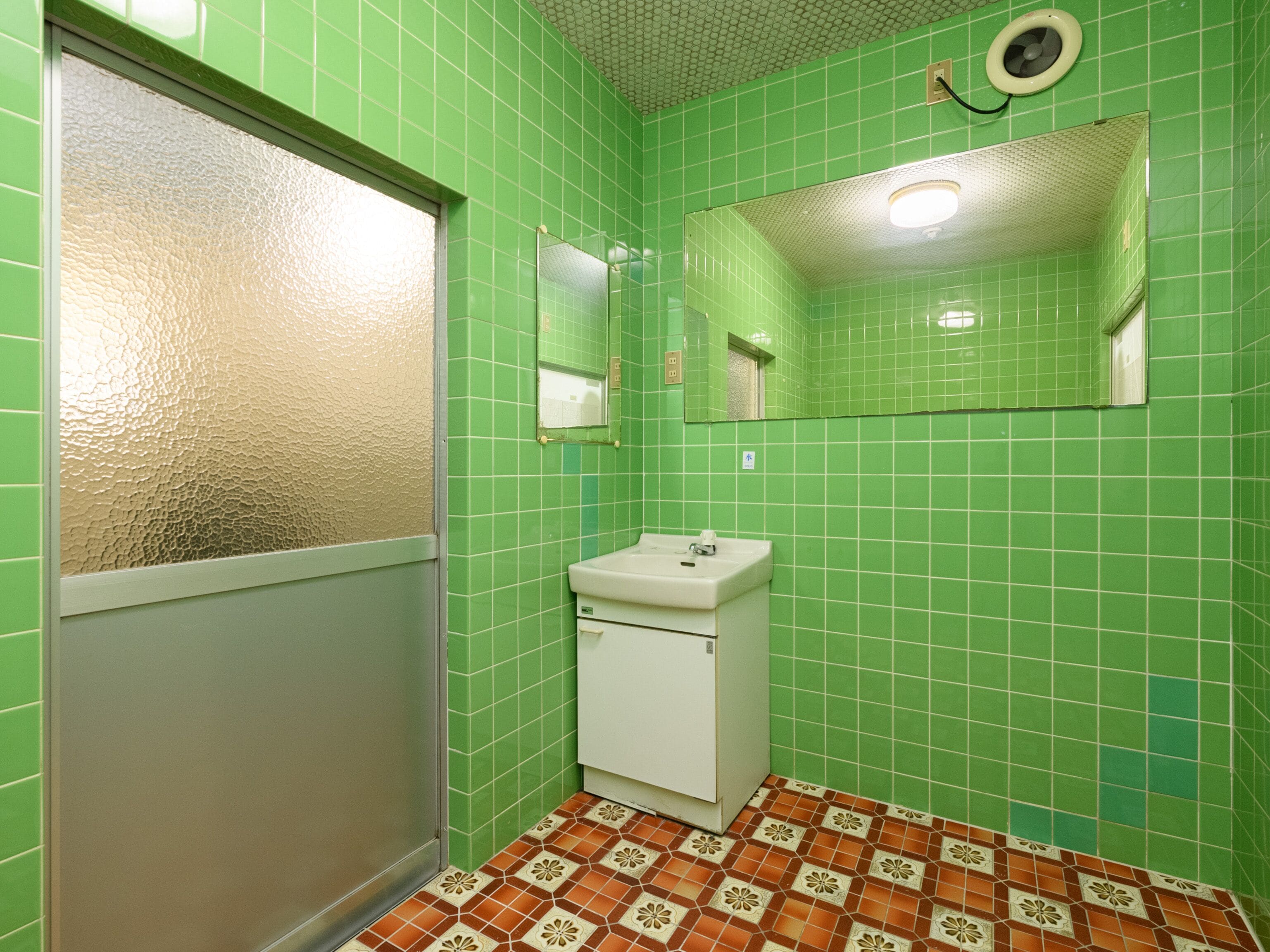 A bathroom with green tiled walls, a white sink, a mirror, and a patterned floor.