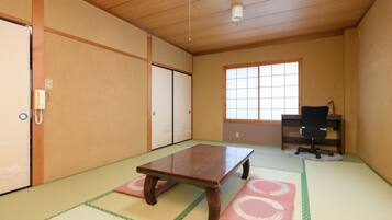 A traditional Japanese room with tatami flooring, a wooden table, sliding doors, a desk with a chair, and a window.