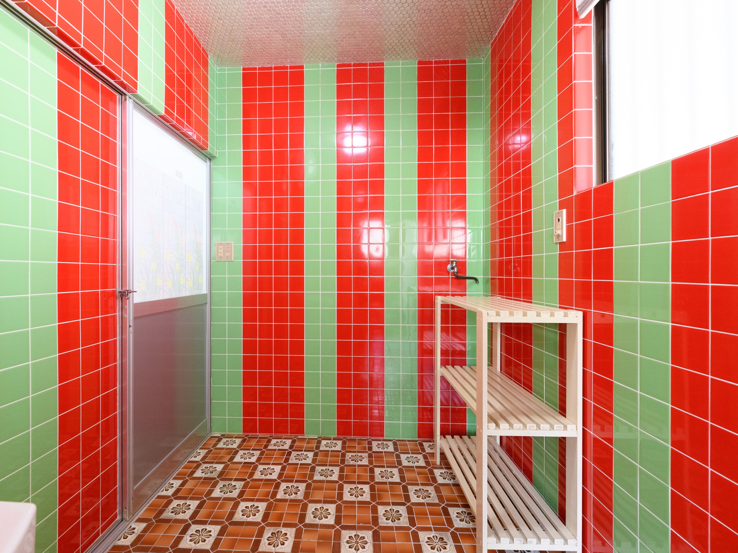 Un baño con baldosas a rayas rojas y verdes, una zona de ducha y un inodoro.