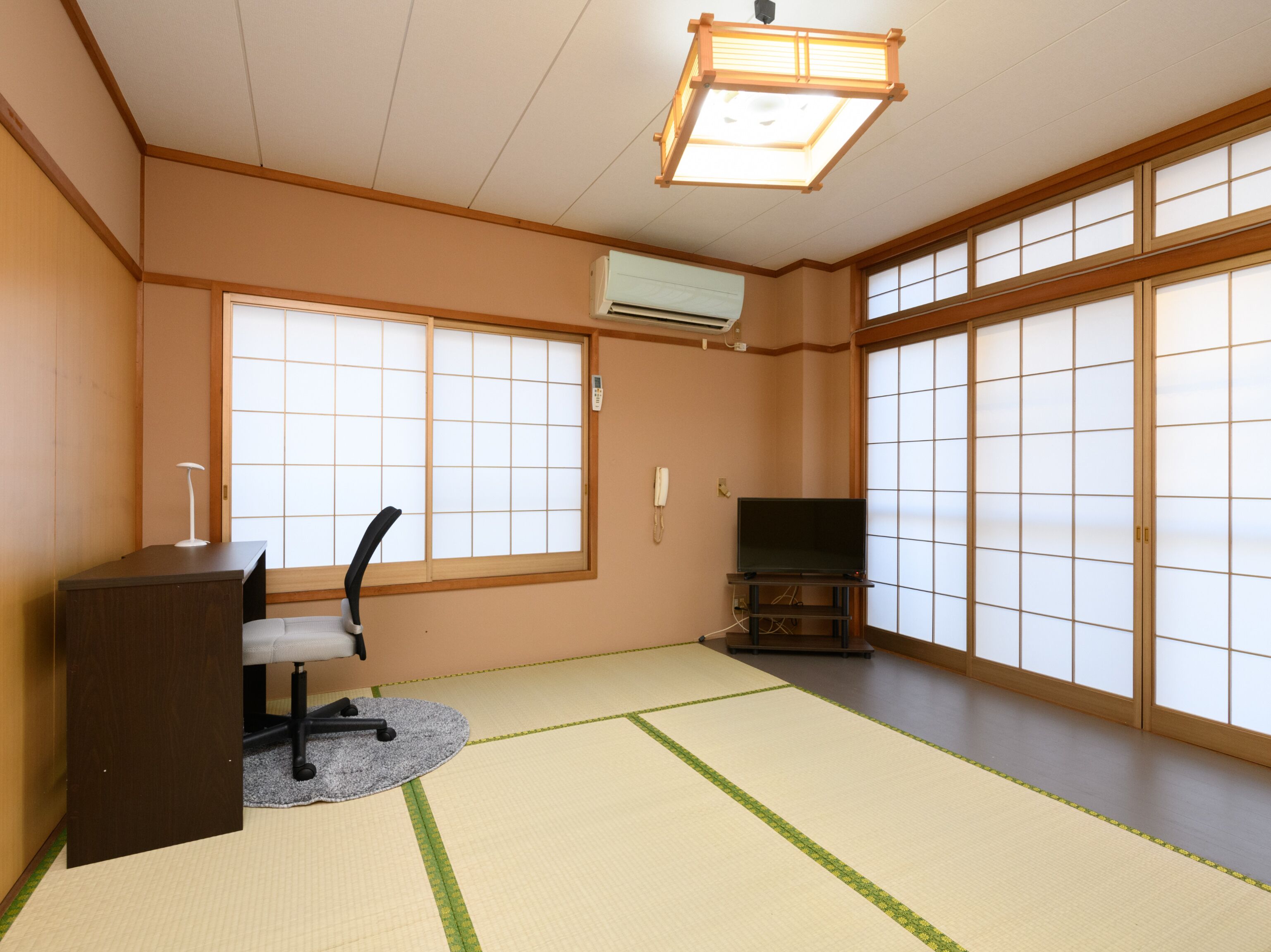 Een traditionele Japanse kamer met tatami vloerbedekking, een bureau met stoel, een televisie en schuifdeuren van shoji-papier.