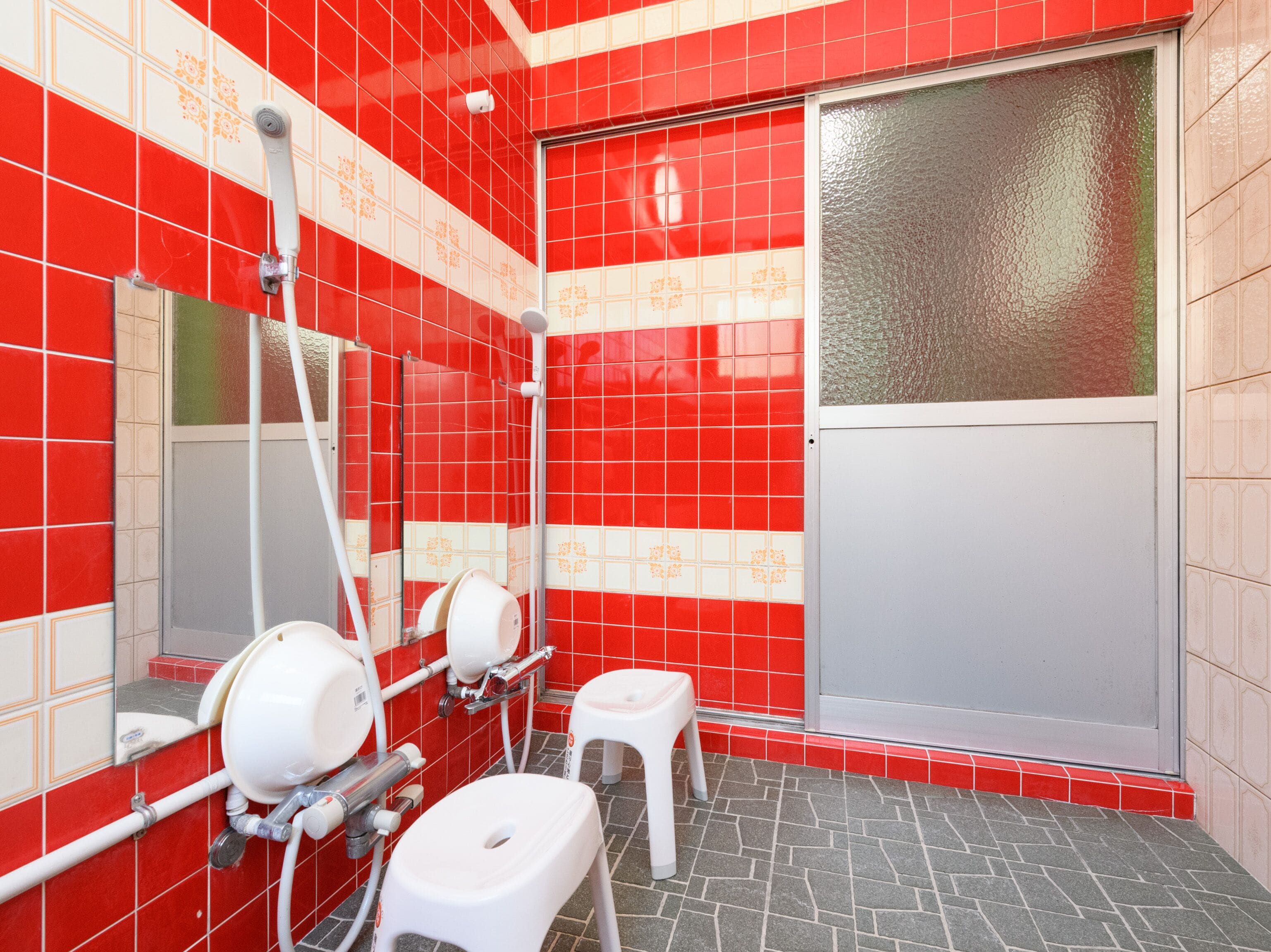 A bathroom with red and white tiles, a glass shower door, a white toilet, and a hand dryer.