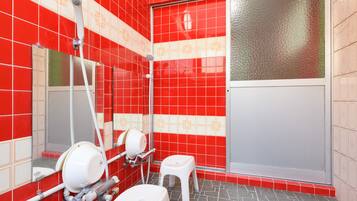 A bathroom with red and white tiles, a glass shower door, a white toilet, and a hand dryer.