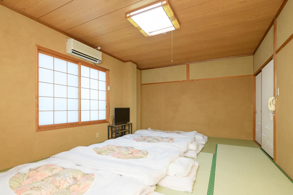 Une pièce de style japonais traditionnel, avec des tatamis au sol, un futon servant de lit, un téléviseur posé sur une petite table et une porte coulissante.