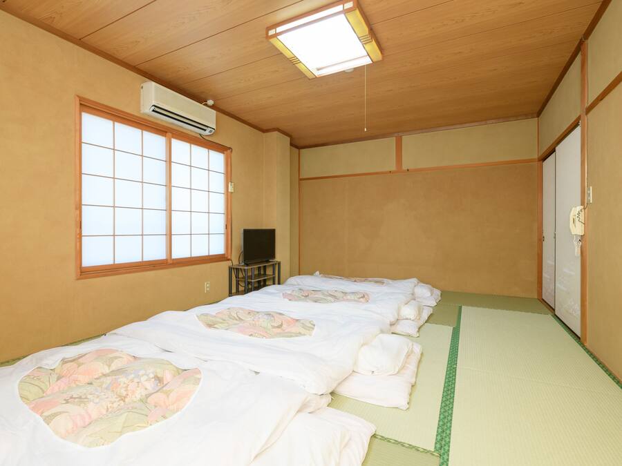Una habitación tradicional japonesa con esteras de tatami, un futón, un televisor sobre una mesa baja y un puertas correderas.