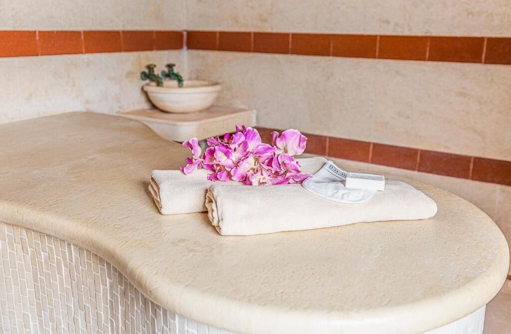Ett spaområde med en beige, strukturerad bänk, en skål med en växt och en handduk med ett blommönster.