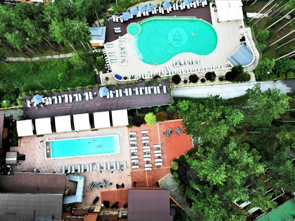 An aerial view of a hotel with two swimming pools, lounge areas, and surrounding greenery.