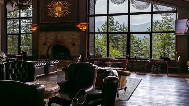 A spacious room with a stone fireplace, leather furniture, large windows with curtains, and a chandelier. - Maxi Park Hotel & Spa (Velingrad)