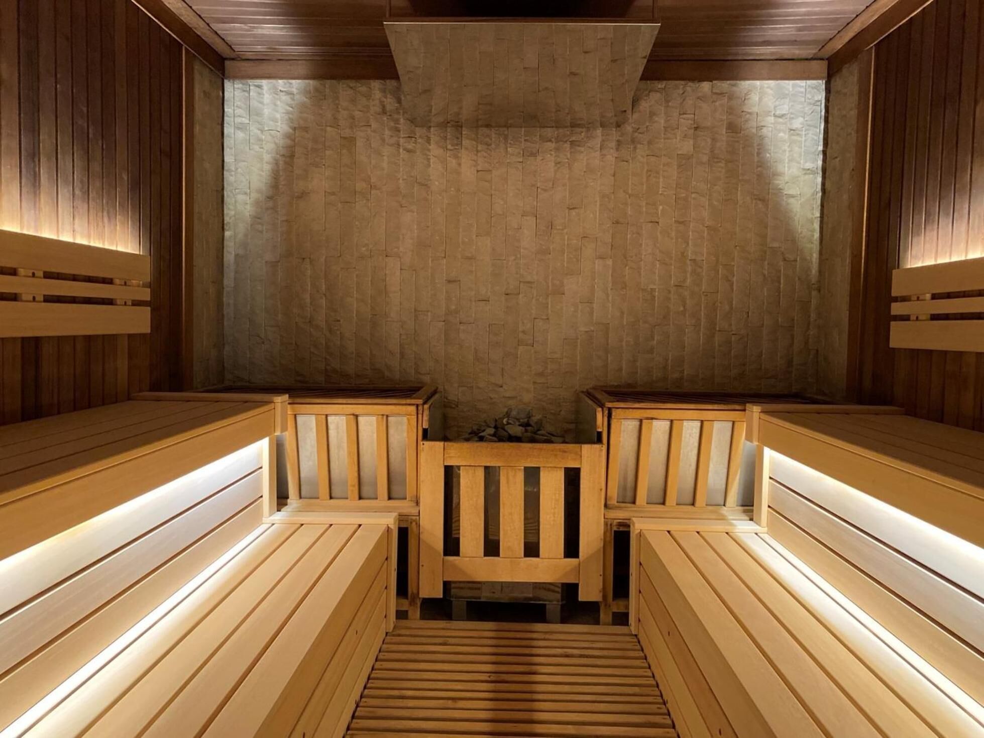 A sauna with wooden benches and benches, a stone wall, and a wooden ceiling.