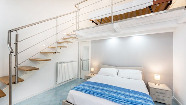 A bedroom with a bed, nightstands, a mirror, a staircase, and a radiator. - Marina Piccola is located in the center of the island, a stone's throw from the beach  (Procida)