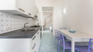 A modern kitchen with white cabinets, a black countertop, and a blue tiled floor. There is a dining area with a white table and purple chairs. - Marina Piccola is located in the center of the island, a stone's throw from the beach  (Procida)