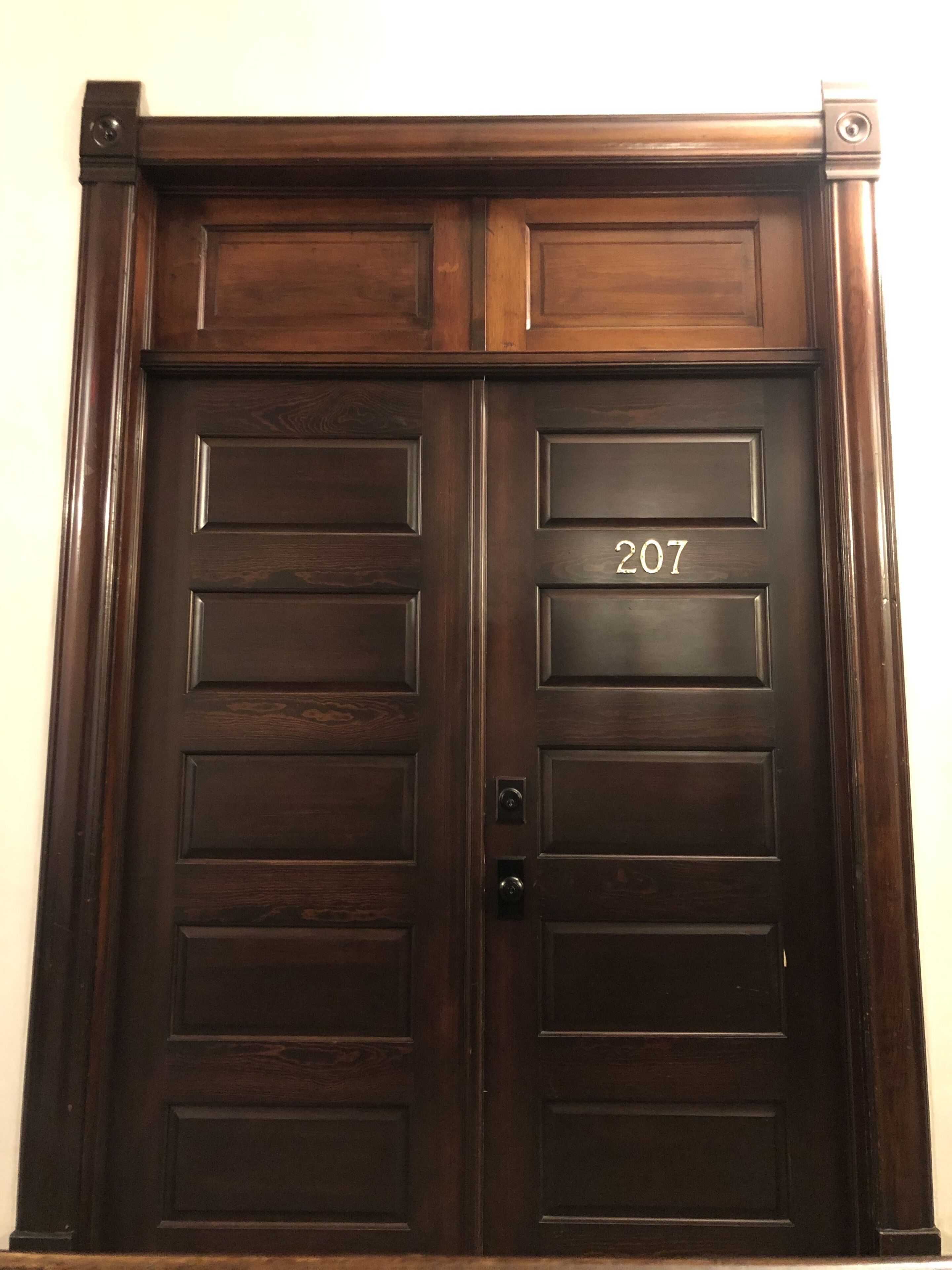 A dark wooden double door with the number 207, indicating a room or unit number.
