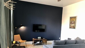 Un salon moderne avec un mur d’accent bleu foncé, un téléviseur à écran plat, un canapé gris, une table basse en bois et une table à manger.