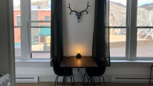 Un coin repas avec une table et des chaises, une décoration murale représentant une tête de cerf et de grandes fenêtres offrant une vue sur les bâtiments et les collines.