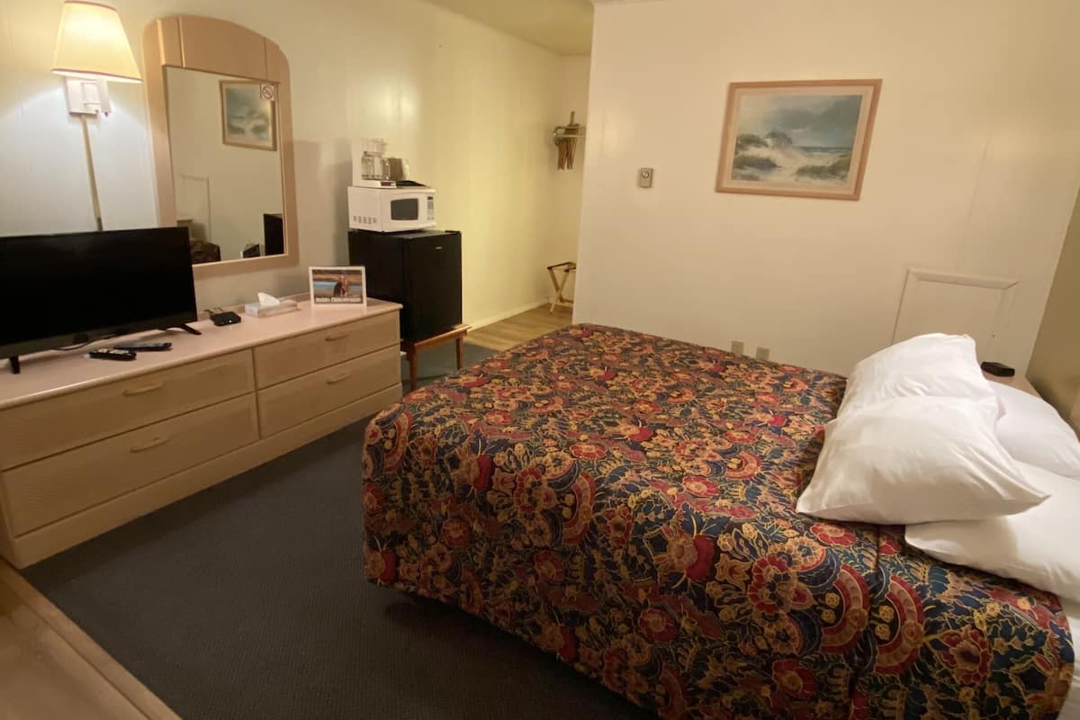 A hotel room with a bed, a dresser, a television, a microwave, and a painting on the wall.