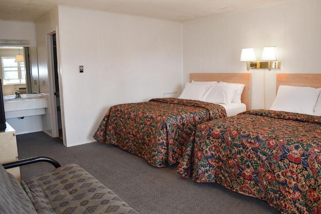 Une chambre d’hôtel avec deux lits, un canapé, une salle de bain avec un miroir et deux lampes fixées au mur.