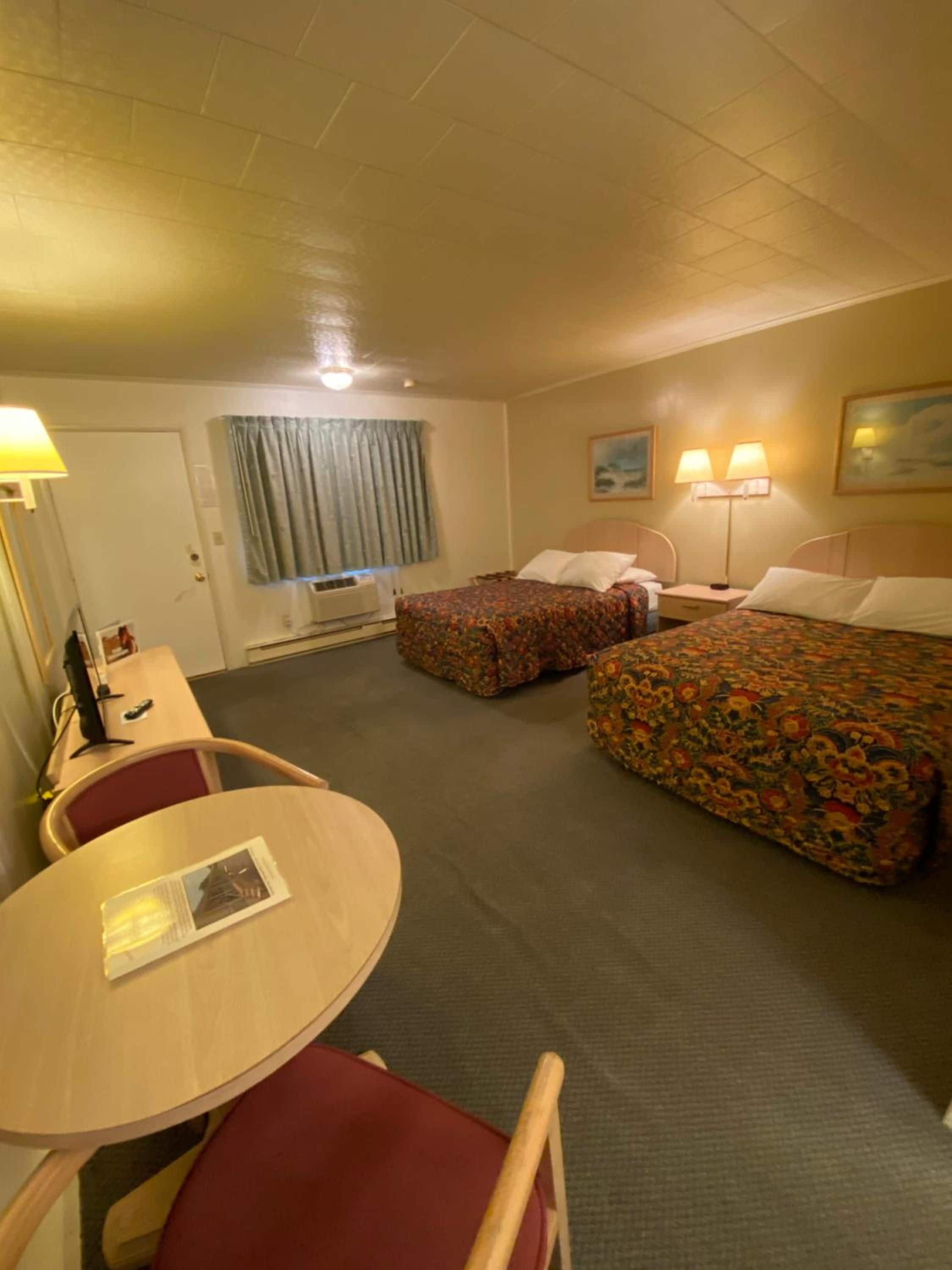 Quarto de hotel com duas camas, uma escrivaninha, uma cadeira e uma mesa.
