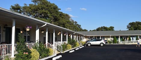 A motel with a covered porch, a parking lot, and a building with a flat roof.