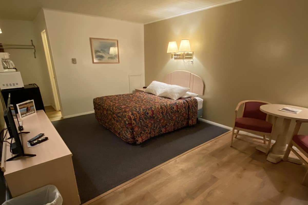 A hotel room with a bed, a desk with a computer, a chair, and a small table.