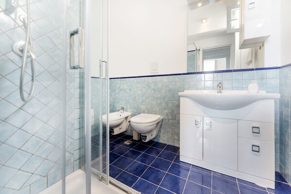 A bathroom with a glass shower enclosure, two toilets, a sink, and a mirror.