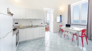 A modern kitchen with white cabinets, a built-in oven, and a dining area with a white table and red chairs. - Fisherman's house in the harbor of Procida (Procida)