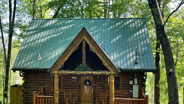 A log cabin with a green metal roof, a front porch with wooden railings, and a wooden door with a wreath. - COZY CABIN!  Perfect Honeymoon or Private Getaway.  Hot tub & Fireplace (Sevierville)
