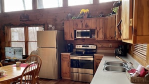 A cozy kitchen with wooden cabinets, a refrigerator, a microwave, an oven, and a dining area with chairs and a table. - COZY CABIN!  Perfect Honeymoon or Private Getaway.  Hot tub & Fireplace (Sevierville)