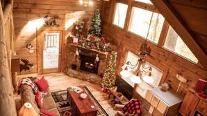 A cozy log cabin interior with a fireplace, a Christmas tree, a sofa, and a dining area. - COZY CABIN!  Perfect Honeymoon or Private Getaway.  Hot tub & Fireplace (Sevierville)