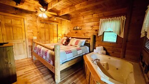 A wooden cabin room with a bed, a wooden ceiling, a ceiling fan, a window with curtains, and a bathtub. - COZY CABIN!  Perfect Honeymoon or Private Getaway.  Hot tub & Fireplace (Sevierville)