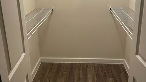 Un dressing accessible sans porte, doté d’un plancher en bois, de murs blancs et d’étagères métalliques.