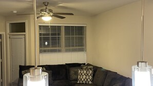Un salon avec un canapé d’angle, un ventilateur de plafond et des luminaires suspendus.